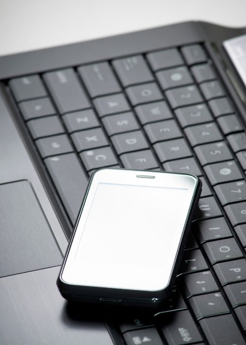 A mobile phone on top of a computer keyboard.